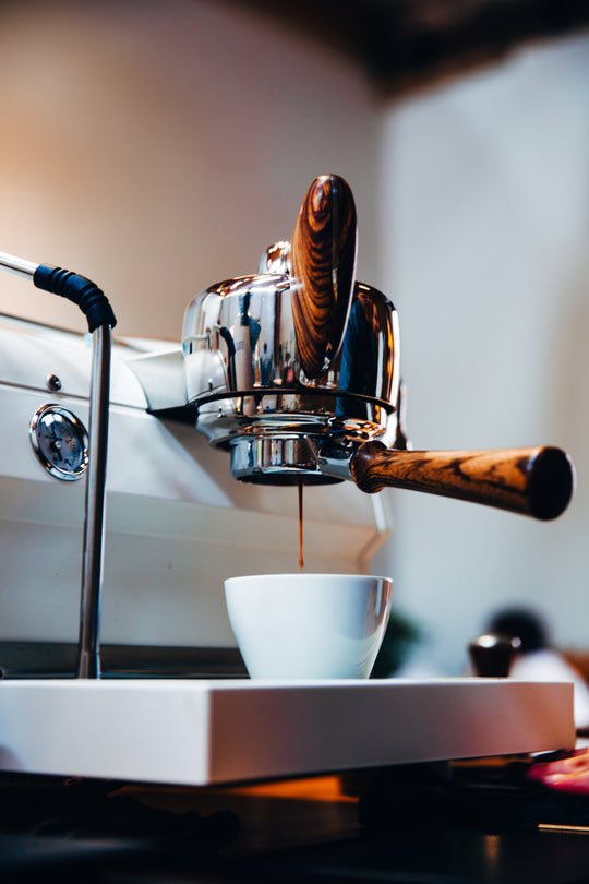 espresso coffee dripping from white slayer espresso machine with maple wood accent